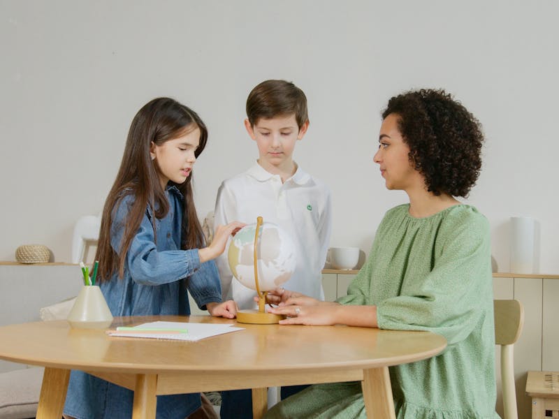 Caregiver and two children exploring a globe together at home